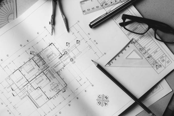 Divider, pencil, pen, ruler, glasses and smartphone and blueprint on table top.Table top view of Engineers table at office workplace.selective focus.Man hand point to blueprint.Black and white effect.